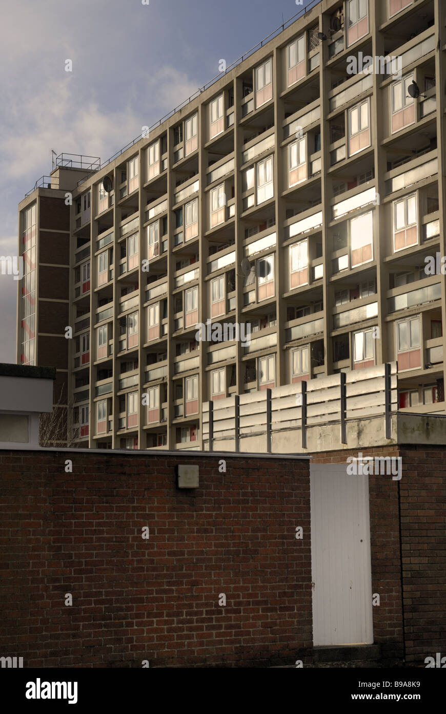 A 1960`s block of flats with light reflecting off windows and a wall and gate in the foreground Stock Photo